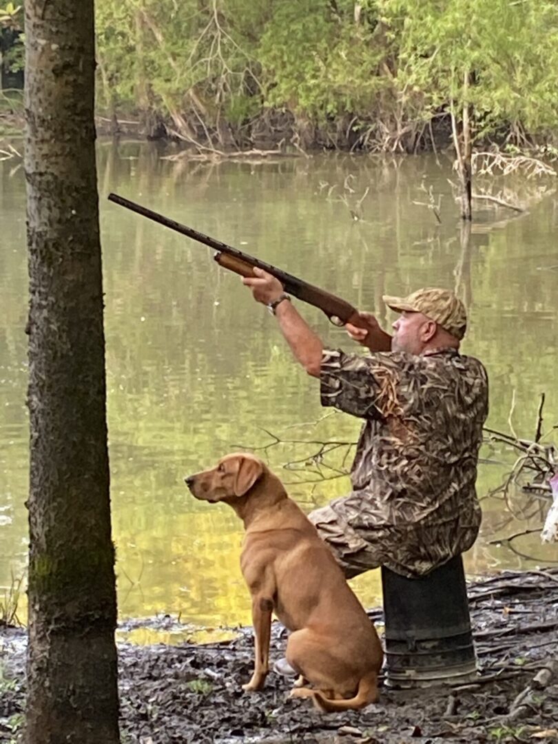 Hunter in camouflage shooting over water with dog